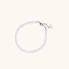 Delicate freshwater pearl bracelet with rhodium-plated silver clasp and single pearl drop charm on cream background