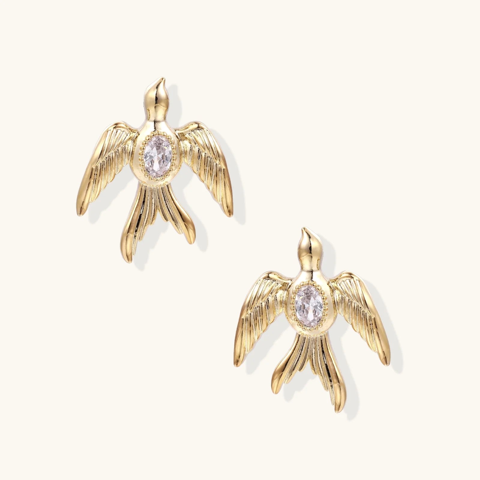 Gold-plated brass earrings shaped as doves in flight with lavender zirconia oval stones at center and textured wing details