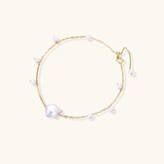Delicate gold chain bracelet with baroque pearl centerpiece and small freshwater pearls on cream background.