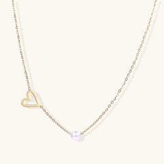 Delicate gold necklace with open heart charm and white pearl bead on fine chain against cream background