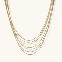 Seven delicate gold-plated snake chains create an elegant layered necklace on a neutral background.