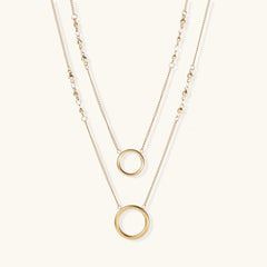 Layered gold necklace set with two open circle pendants and mixed chain styles on beige background
