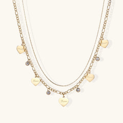Gold layered necklace set with engraved heart pendants and crystal accents on cream background