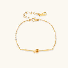 Delicate gold chain bracelet with minimalist bar and centered knot detail on cream background