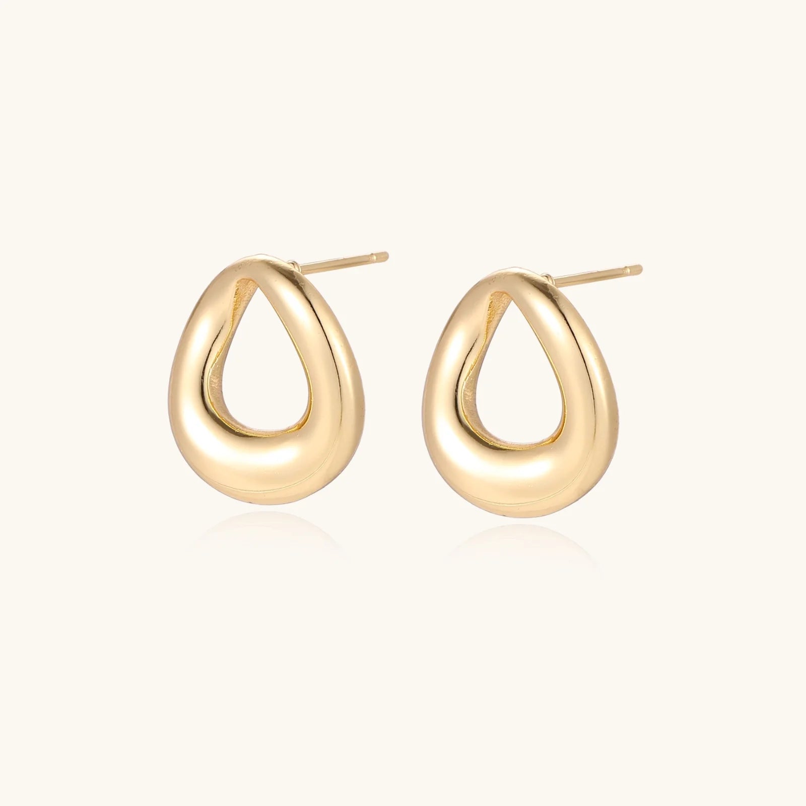 Pair of polished 18K gold-plated stainless steel teardrop earrings with hollow centers on cream background
